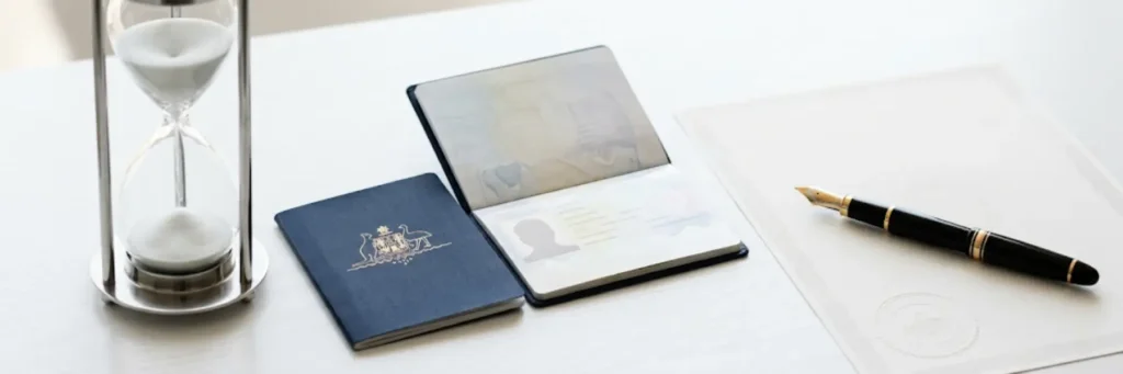 Hourglass, Australian passport open and closed, fountain pen on white document on a white table.